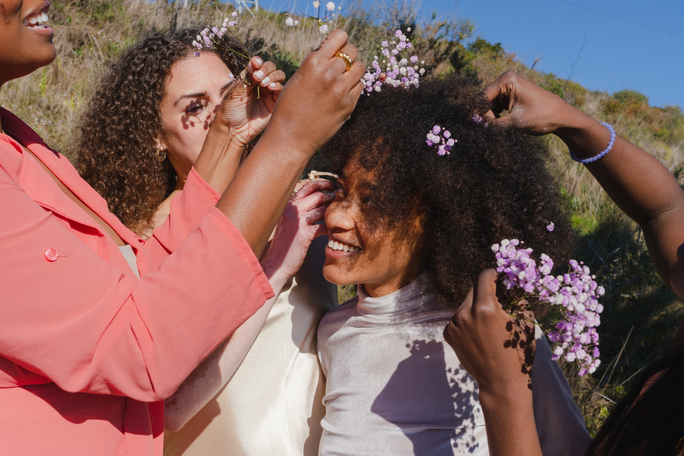 Women Putting Flowers in Woman's Curly Hair